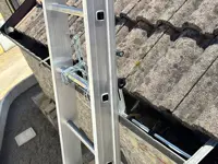 Accesorio de fijación de escalera en su parte superior a: bordes, vallas publicitarias, canalones 